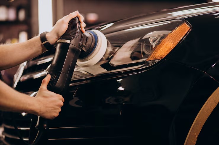 Professional car detailer polishing a glossy black vehicle near the headlight
